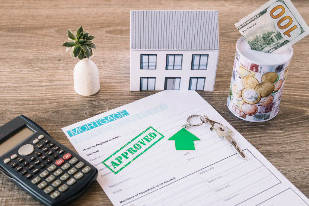 Approved mortgage form with house model, calculator, keychain, and money jar on a table